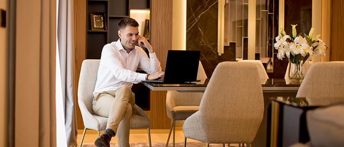 A man working at a table with a laptop in a luxurious residence.