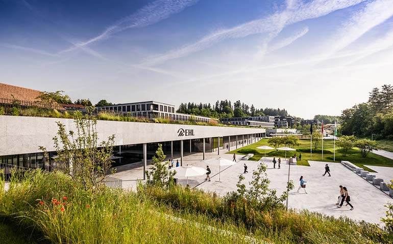 Green landscape with a building in the center and students entering the EHL building