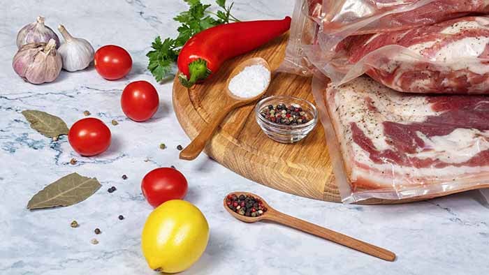 A wooden cutting board displaying an assortment of sous vide beef, vibrant vegetables, and various spices arranged artfully