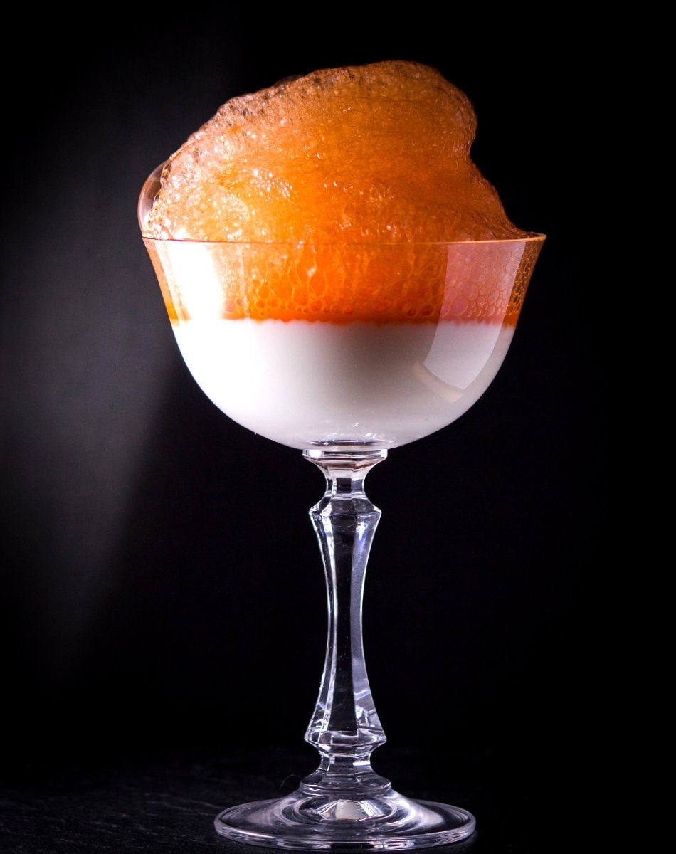 Orange foam atop a cloudy cocktail