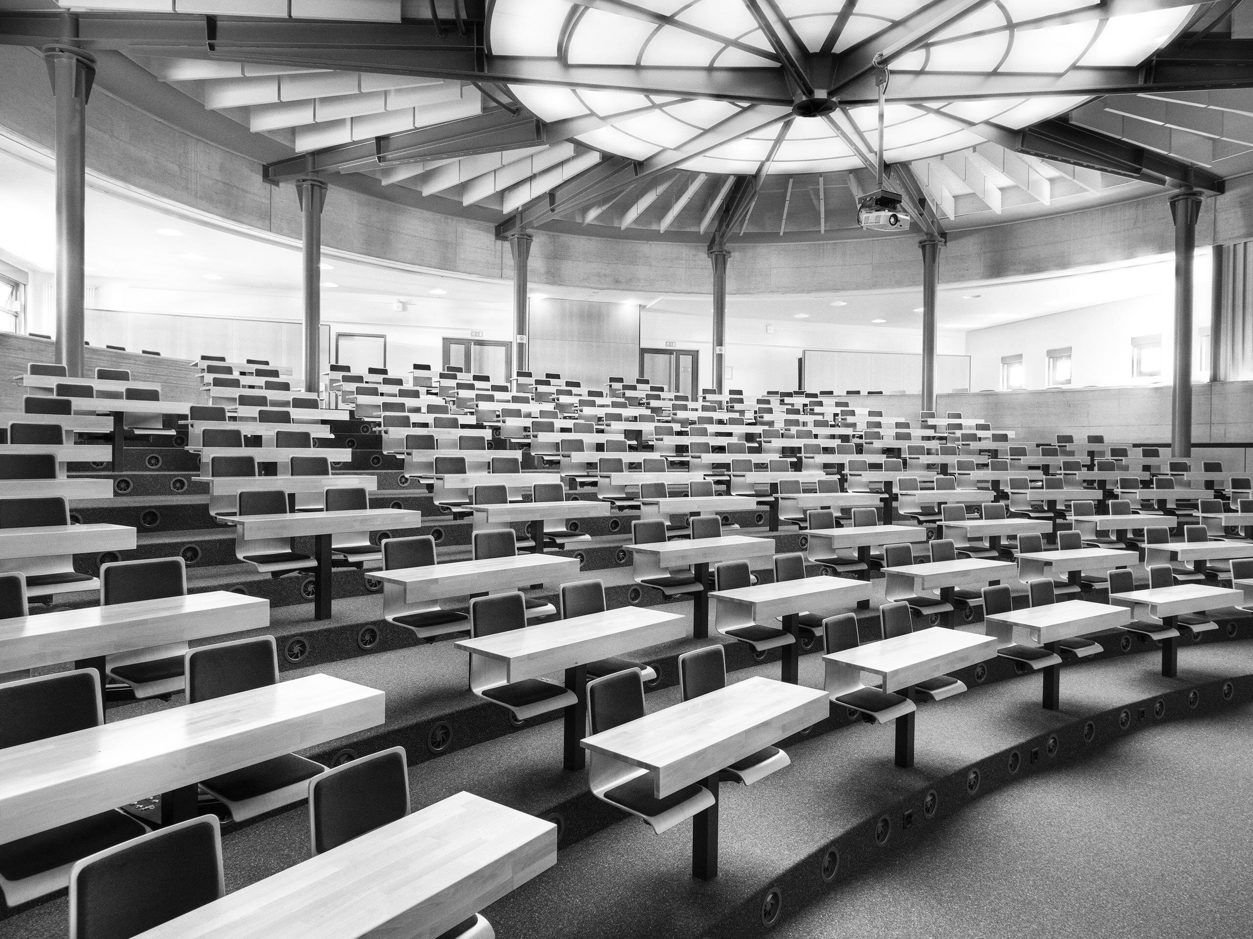 A monochrome image of a lecture hall with neatly arranged rows of chairs