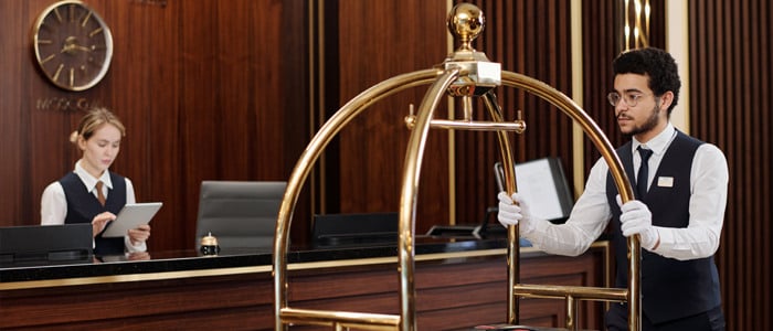 a man and woman stand at a hotel reception desk,