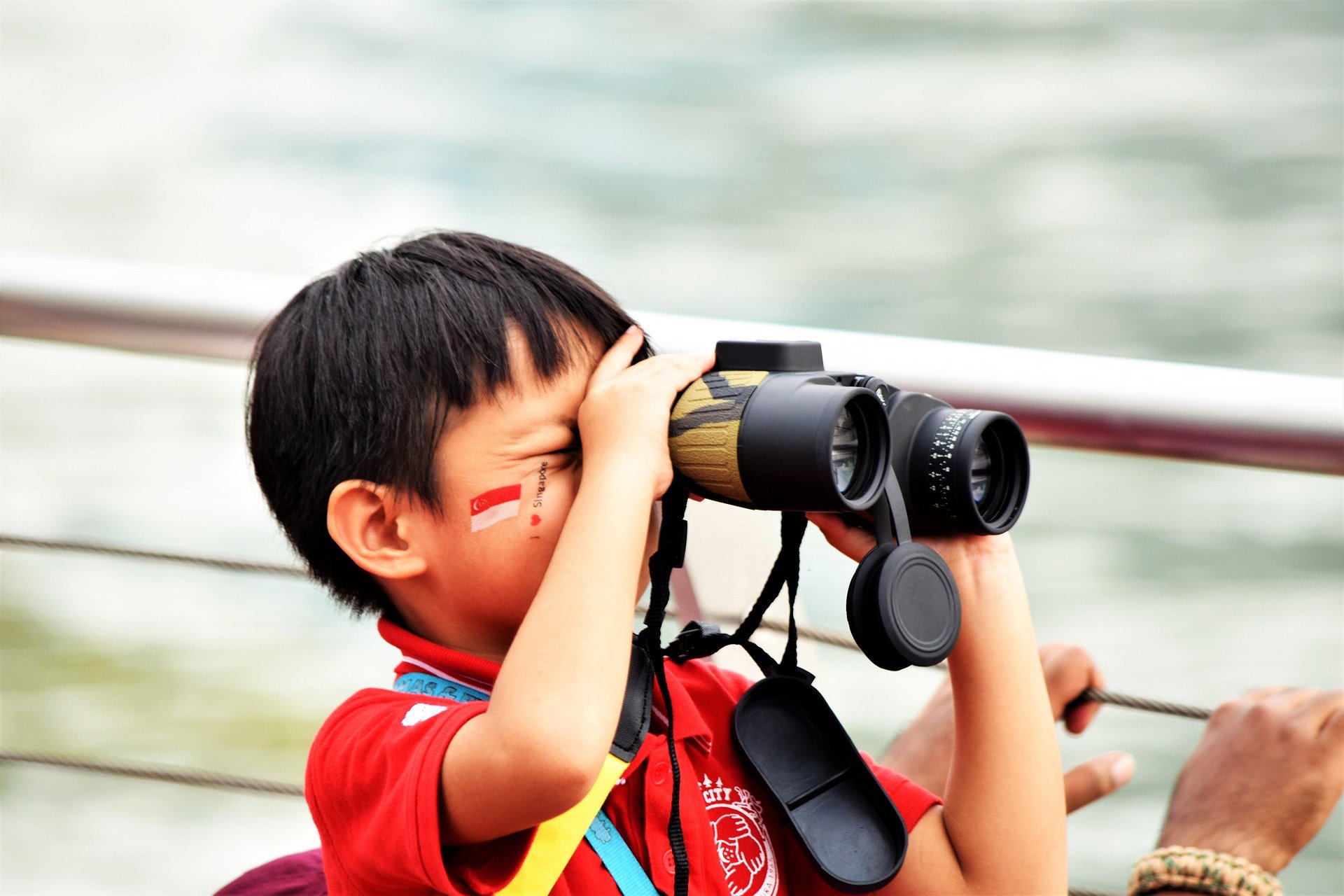 A kid with the Singaporean flag painted on his face looing through binoculars