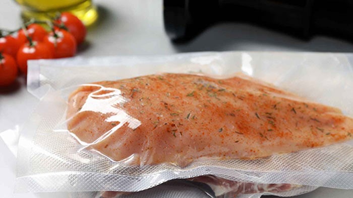 A piece of chicken placed inside a bag - sous vide, alongside fresh, ripe tomatoes